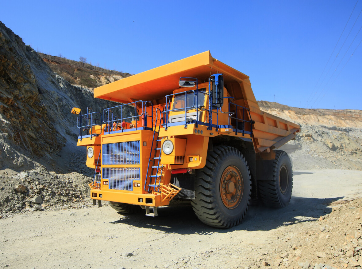 Large yellow mining dump truck on the road on a sunny day. Large-sized equipment for the transportation of rock mass in an ore quarry.